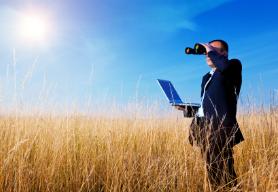picking a domain name in a field on laptop with binoculars